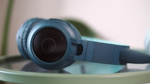 A close-up view of blue over-ear headphones resting on a green glass table surface.