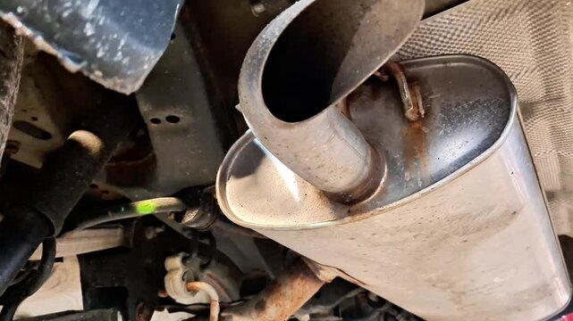 Underside view of vehicle exhaust system showing cylindrical muffler, connected pipes, and chassis details, highlighting automotive mechanics, repair context, and structural components