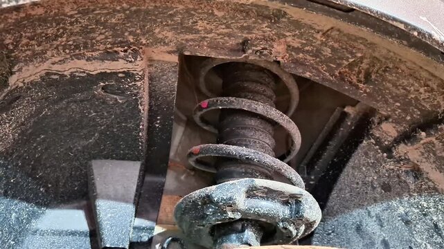 Close up of vehicle suspension with coil spring and shock absorber above wheel, showing dirt covered components in working condition, highlighting automotive repair and maintenance context