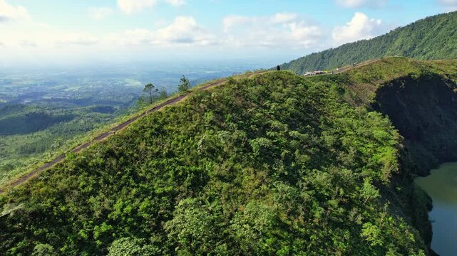Aerial drone footage of the edge of Galunggung volcano mountain crater, at early sunrise, with vegetations, food stalls, with Tasikmalaya city behind far away, in Java island, Indonesia