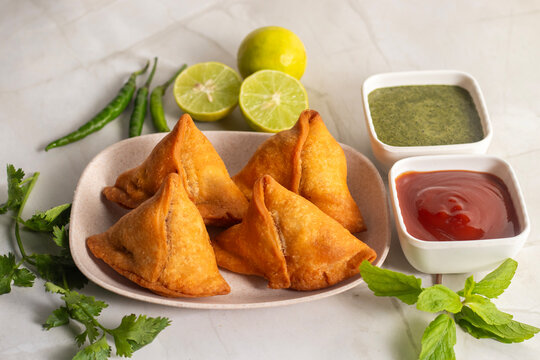 Crispy golden samosa served with mint chutney tomato sauce fresh lemon on wooden board Indian street food snack delicious appetizer
