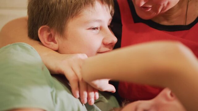 Playful kitchen cuddle white home cook mother playfully shushing and smiling at son on couch, gentle hand gesture, apron visible, cozy warm light, affectionate teasing and comforting family moment.