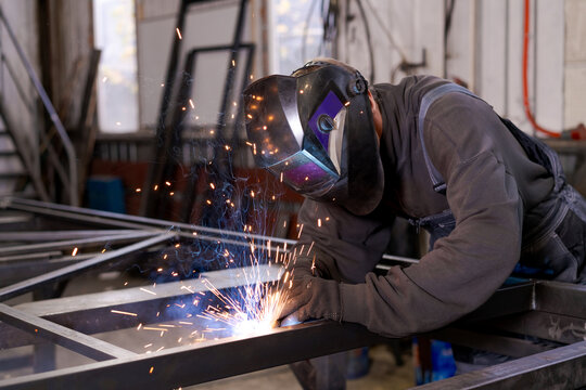 Welder in Protective Mask Welding Steel Frame with Sparks