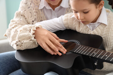 Fototapeta premium Little girl with music teacher learning to play guitar at home, closeup