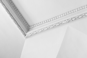 Elegant white interior showing a decorative plaster ceiling corner with ornate molding and classic cornice detail. Minimal composition emphasizes texture, symmetry and historic architectural charm © evannovostro