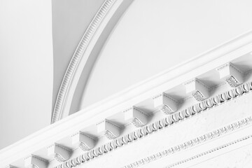 Bright, high-key close-up of an elegant white ceiling cornice and arch showing ornate plaster molding, highlighting classical architectural detail and refined interior design © evannovostro