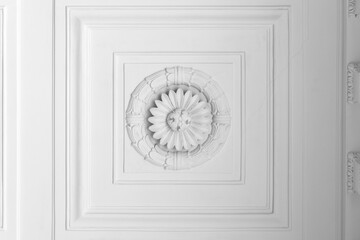 White plaster ceiling rosette surrounded by layered decorative molding and framed panels, showcasing classic architectural ornament, symmetrical floral relief and elegant historic interior details © evannovostro