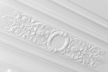 White decorative plaster ceiling molding featuring an ornate circular medallion and intricate floral relief scrollwork, highlighting classic architectural detail, elegant texture and vintage interior © evannovostro