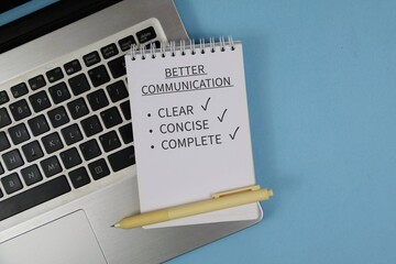 Notepad reading “Better Communication” with checklist items clear, concise and complete sits on a laptop keyboard beside a pen on blue background, conveying workplace communication and productivity. © Ilyas