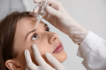 Naklejka premium Woman receiving cosmetic eye drops during ophthalmology examination in clinic, close up of patient with gloved doctor hands applying treatment to eye