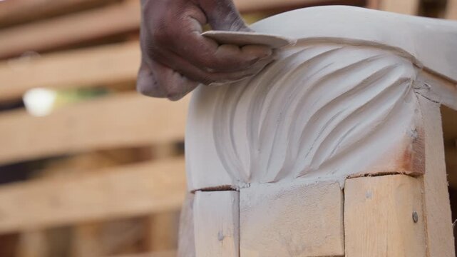 Closeup black hands sanding carved molding, apprentice restorer in carpentry workshop, gentle strokes with sanding block on ornate corbel, dusty texture, warm pallet background, focused patience