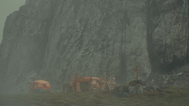 Remains of Russian research base with orange shelters, red cross markers and wooden equipment sit at base of towering sheer cliff at Point Wild, Elephant Island, in swirling geothermal mist