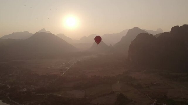 Following aerial view of large red hot air baloon in the sky during sunset with tropical mountainous landscape in the background. No visible logos.