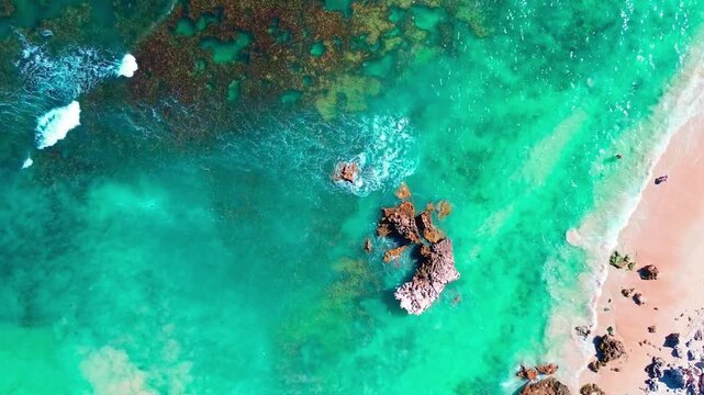 Breathtaking drone shot of crystal clear emerald sea water swirling around coral reefs and shoreline.
