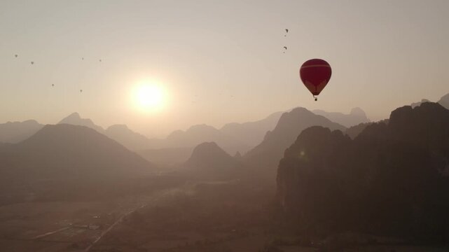 Vang Vieng, Laos - February 16, 2026: Hot air baloons and paragliders flying around the city of Vang Vieng during late afternoon.