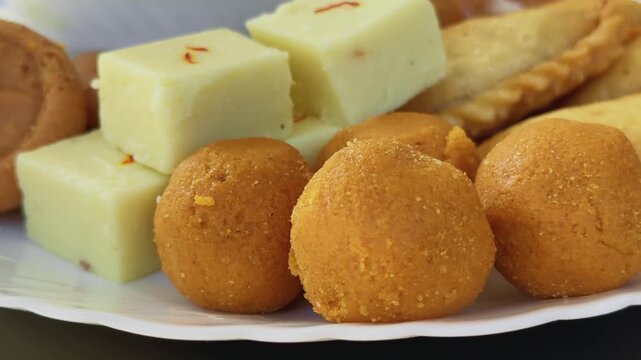 Turntable closeup highlighting soft, grainy-textured besan laddu in the foreground emphasizing rich color, texture, and festive indulgence.