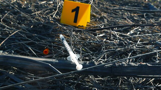 Forensic evidence marker number one indicating a used syringe on the ground at a crime scene, symbolizing a narcotics related investigation or overdose death in an outdoor setting