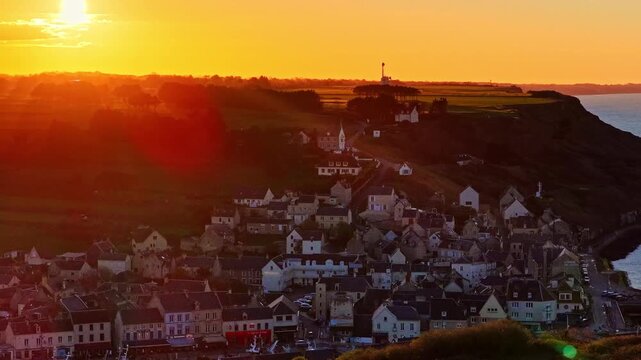A slow pullback drone view of the village of Port en Bessin under a bright orange sunset.