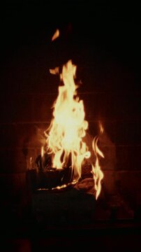 Close-up slow motion of fire burning in a fireplace. Warm glowing flames and wood logs. Flames dancing. Warm light create cozy, intimate mood.