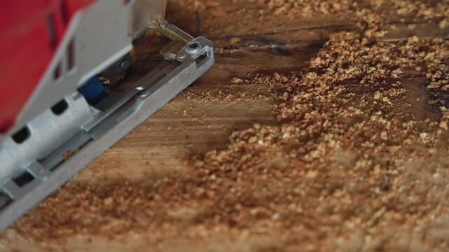 Final pass jigsaw across timber surface, satisfying finishing cut with abundant sawdust texture and smooth grain reveal, cabinetmaker finishing touch on bench, closeup of blade base and motor housing