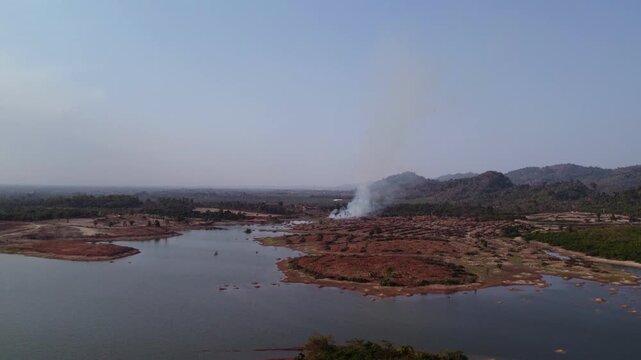 Aerial forward moving flying view of agricultural burning field during the slash and burn dry season in the countryside of Laos.