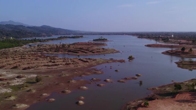 Forward aerial view of sand patches along the coastline of lake during dry season with hazy polluted air in the background.