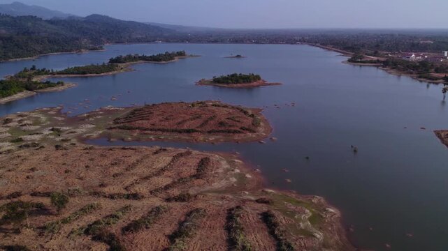 High altitude slow forward aerial view of sand patches along the coastline of lake during dry season with hazy polluted air in the background.