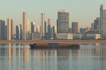 Fototapeta premium Container barge navigates river in China with city skyline in background at daytime