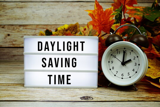 Daylight Saving Time text with alarm clock and maple leaf decoration on wooden background