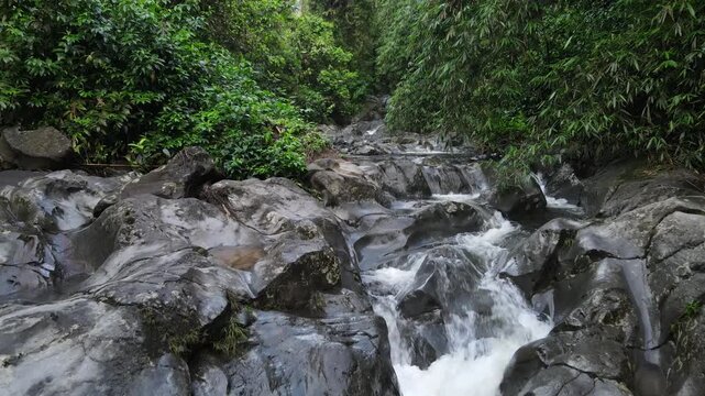 Aerial view of Small waterfall cascading over smooth stones in a tropical jungle, Clear mountain stream running through a rocky riverbed. babbling brook and vibrant green foliage.