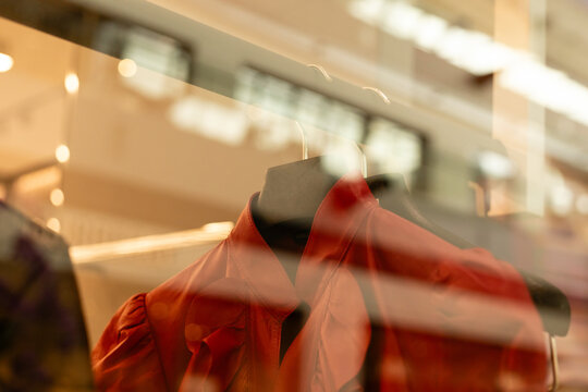 Clothing hangs on a rack inside a store window. Light reflects off the glass, creating an interesting view of the items on display in a shopping area