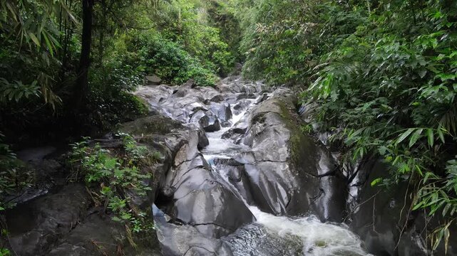 Aerial view of Small waterfall cascading over smooth stones in a tropical jungle, Clear mountain stream running through a rocky riverbed. babbling brook and vibrant green foliage.