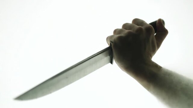Silhouetted hand holding a sharp knife against a bright white background, creating a scary mood