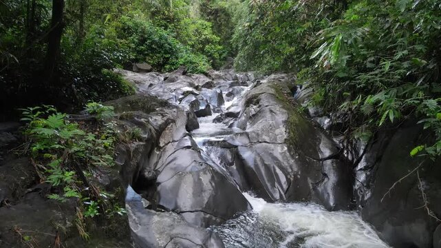 Aerial view of Small waterfall cascading over smooth stones in a tropical jungle, Clear mountain stream running through a rocky riverbed. babbling brook and vibrant green foliage.