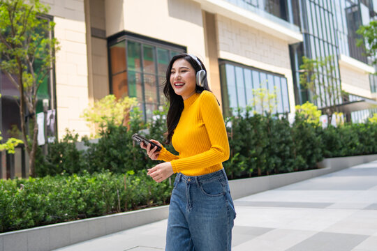 Asian woman enjoying music with headphones while standing in the city.