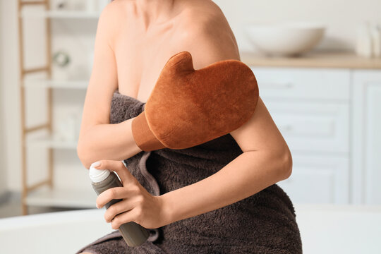 Young woman with massage glove applying self tanner mousse in bathroom, closeup
