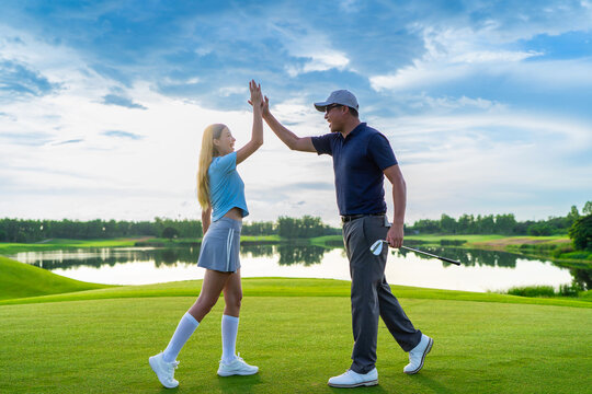 Asian man and woman golfers making a high five on scenic golf course. 