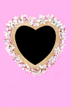 Heart shaped apple blossom springtime wreath with wooden frame on pink. Romantic symbol of love for Mothers Day, Beltane, Valentines, birthday, wedding.