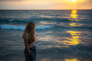 Fototapeta premium A woman stands relaxing by the sea in the evening as the sun sets.