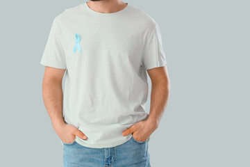 Obraz premium Young man with blue ribbon on light background. Prostate cancer awareness concept