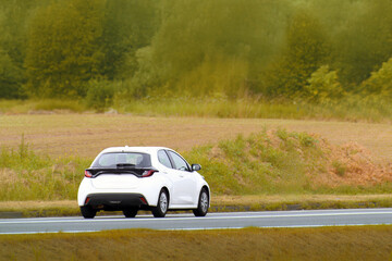 Fototapeta premium Urban hatchback driving through open green fields