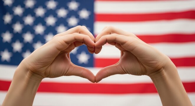 Hands forming a heart shape in front of a waving american flag symbolizing patriotism
