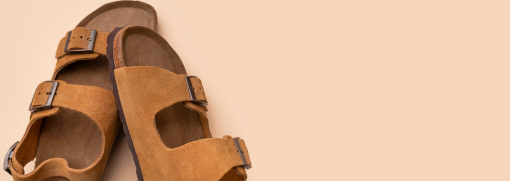 Stylish summer leather sandals on gray background, top view. Brown unisex flip-flops made of genuine nubuck leather with cork sole for beach and travel. Fashionable footwear, minimalist layout