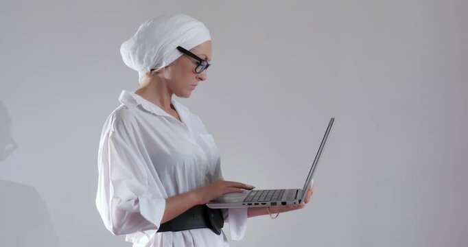 Business goal-oriented young woman in glasses and a turban with a laptop in her hands at work