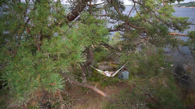 Couple relaxing in hammock by lake, authentic outdoor moment in wild nature, mental health and sustainable travel concept, natural light.