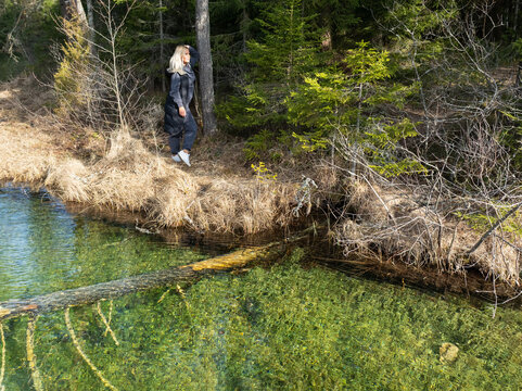 Blonde woman standing by the crystal clear turquoise water of Antu lake in Estonia forest, enjoying pristine nature and serenity.