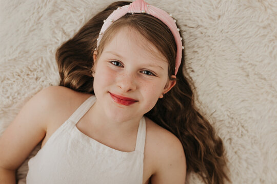 Young girl with blue eyes lays on blanket while looking at camera