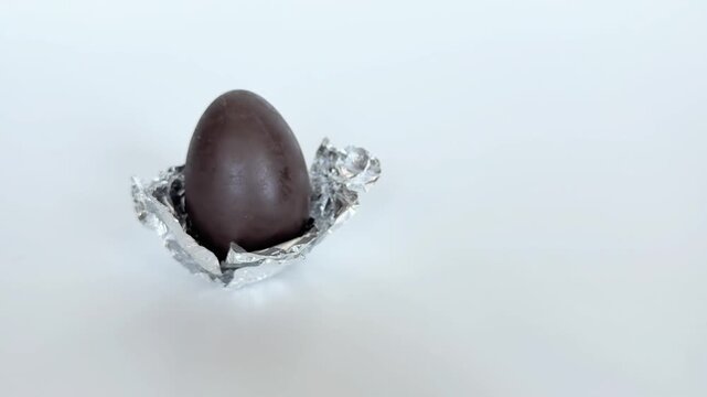 Single chocolate egg wrapped in foil on silver wrapper, close up on white background. Chocolate egg, foil, wrapper, white, single, close up
