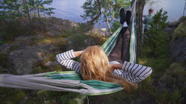 Couple relaxing in hammock by lake, authentic outdoor moment in wild nature, mental health and sustainable travel concept, natural light.