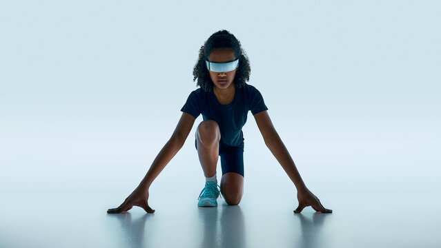 Teen athlete in starting pose wearing reflective futuristic visor in minimal studio background. Concept of sport technology, performance tracking innovation, and future fitness training.